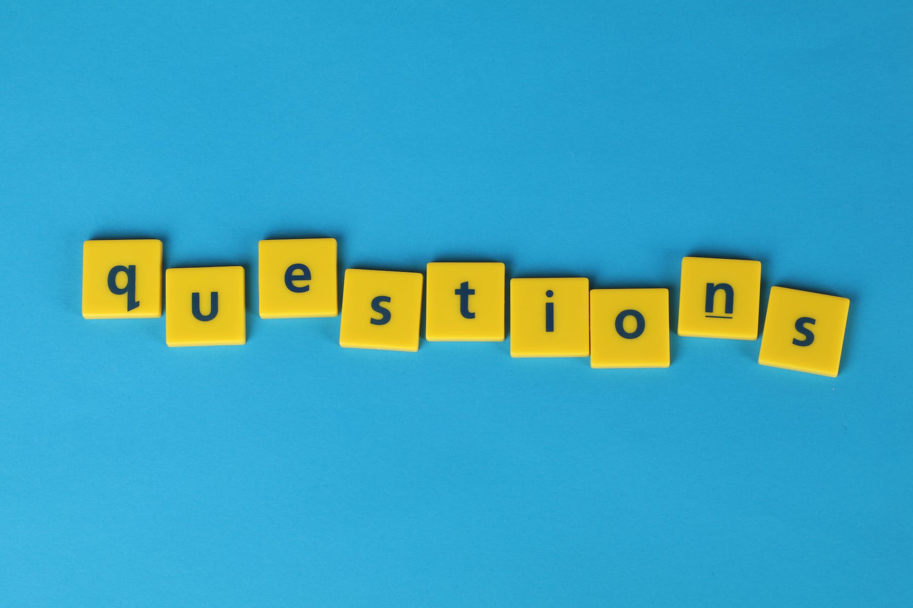 Yellow tiles with black letters spelling "questions" are arranged in a horizontal line against a blue background, resembling the clarity needed for an effective FAQ section.